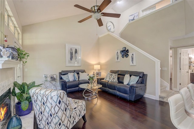 living area featuring wood finished floors, a towering ceiling, a glass covered fireplace, ceiling fan, and stairs