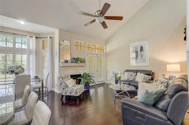 living area with baseboards, ceiling fan, a tiled fireplace, wood finished floors, and high vaulted ceiling