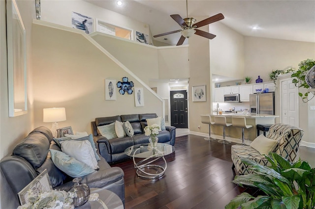 living room featuring a ceiling fan, baseboards, high vaulted ceiling, stairs, and dark wood-type flooring