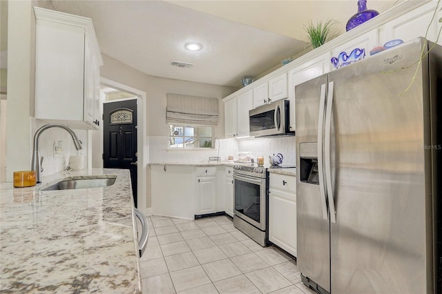 kitchen with visible vents, light stone counters, stainless steel appliances, white cabinetry, and a sink