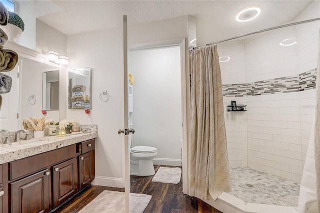 full bathroom with toilet, tiled shower, vanity, and wood finished floors