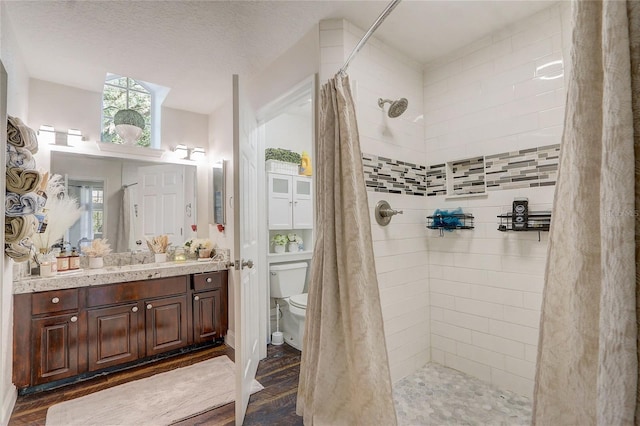 bathroom featuring toilet, a textured ceiling, wood finished floors, a tile shower, and vanity