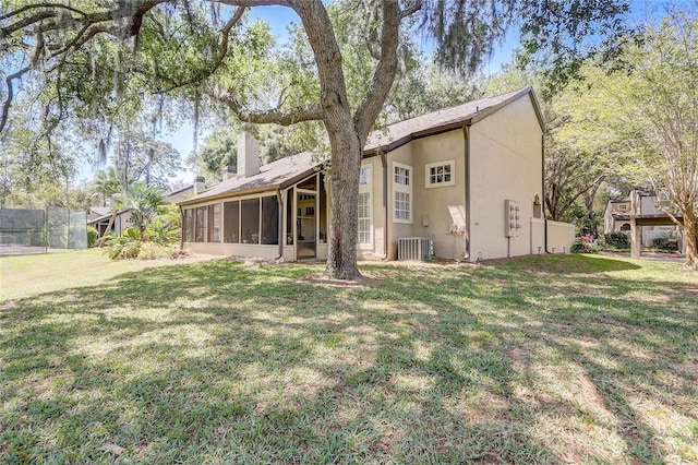 back of house with stucco siding, a lawn, a chimney, and a sunroom