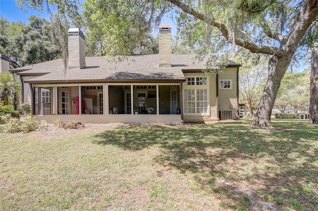 back of house featuring a lawn, a chimney, a sunroom, and stucco siding