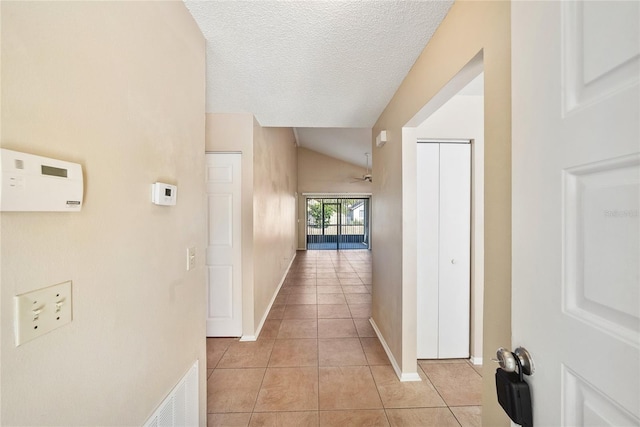 corridor featuring light tile patterned floors, baseboards, visible vents, and a textured ceiling