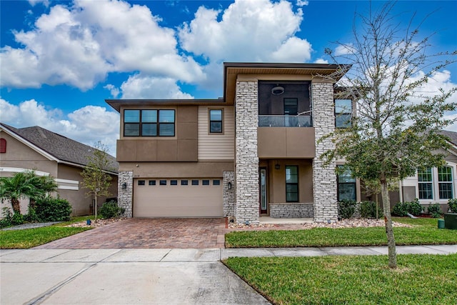 view of front of home featuring stone siding, stucco siding, decorative driveway, and a balcony