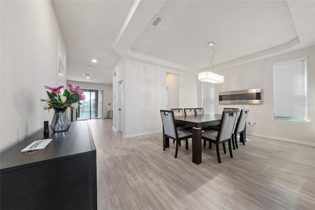 dining space featuring visible vents, baseboards, a raised ceiling, and light wood-style floors