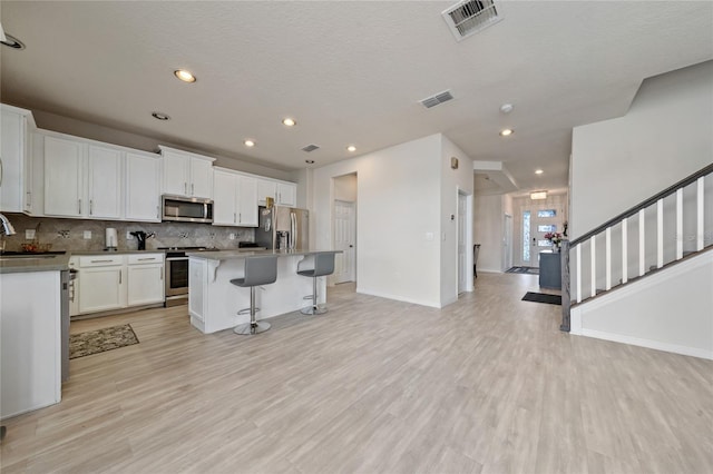 kitchen featuring visible vents, backsplash, light wood-style floors, stainless steel appliances, and a sink