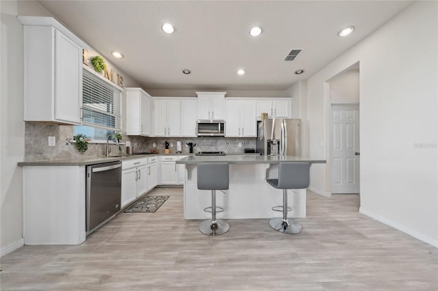 kitchen featuring visible vents, a kitchen island, appliances with stainless steel finishes, white cabinetry, and a kitchen breakfast bar