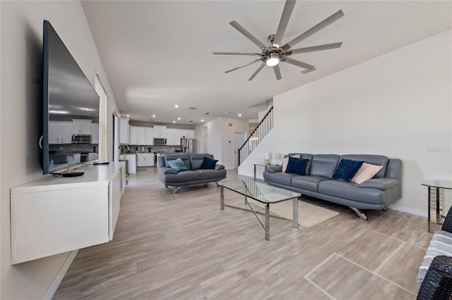 living room featuring baseboards, light wood-type flooring, stairs, recessed lighting, and a ceiling fan