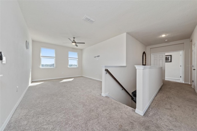 carpeted spare room with visible vents, a textured ceiling, baseboards, and ceiling fan