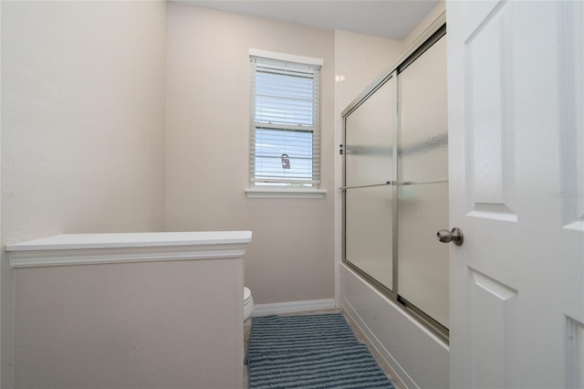 full bathroom featuring combined bath / shower with glass door, baseboards, and toilet