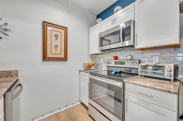 kitchen with stainless steel appliances, light wood-style floors, white cabinets, a toaster, and decorative backsplash