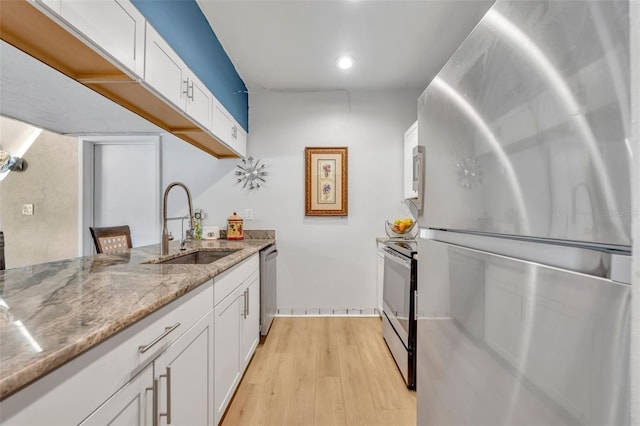 kitchen featuring light stone countertops, stainless steel appliances, light wood-style floors, white cabinetry, and a sink