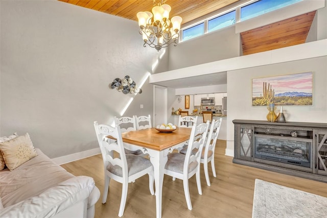 dining area featuring baseboards, wooden ceiling, a high ceiling, light wood-style floors, and an inviting chandelier