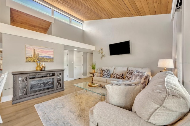 living area featuring a towering ceiling, wood ceiling, baseboards, and wood finished floors