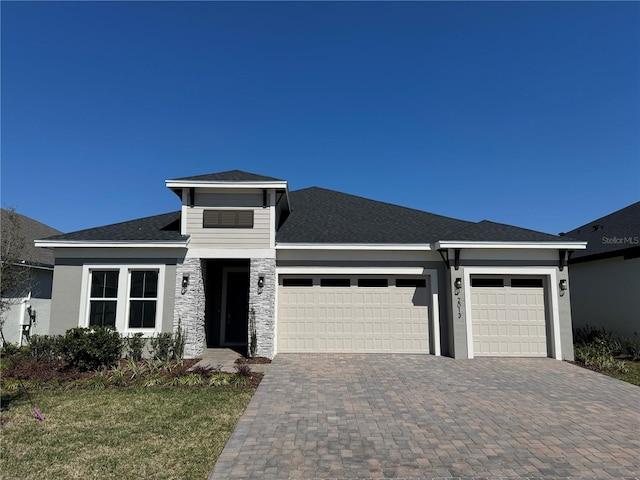 prairie-style home with decorative driveway, an attached garage, a shingled roof, and stucco siding