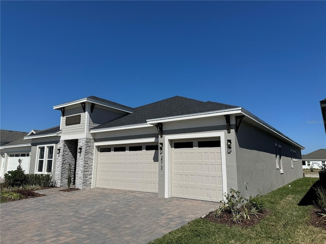 view of front facade with decorative driveway, stone siding, an attached garage, and stucco siding