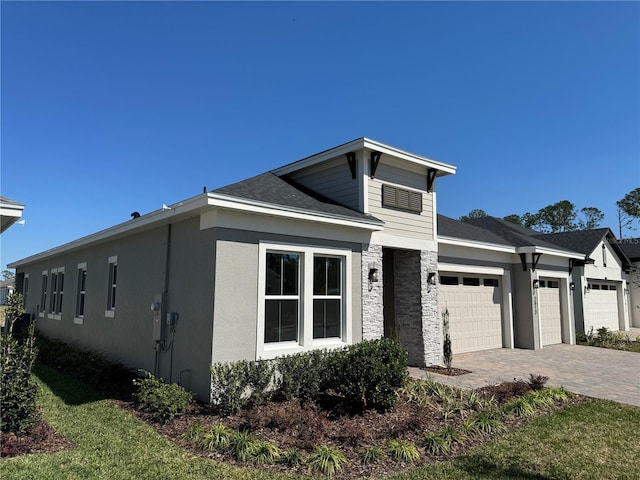 view of front of home featuring stone siding, a garage, decorative driveway, and stucco siding