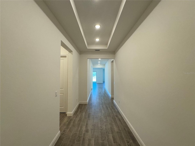 hall featuring dark wood-style floors, recessed lighting, a raised ceiling, and baseboards