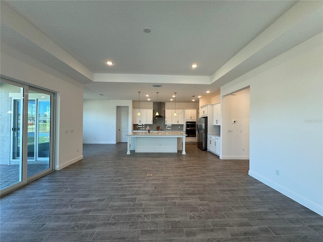 kitchen featuring stainless steel fridge with ice dispenser, light countertops, white cabinetry, wall chimney range hood, and open floor plan