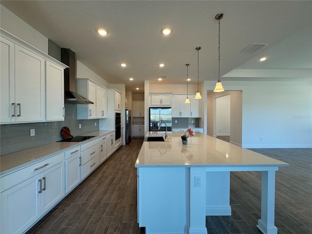 kitchen with wood finish floors, wall chimney range hood, white cabinets, black appliances, and a sink