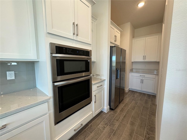 kitchen featuring light stone countertops, wood finish floors, decorative backsplash, white cabinets, and appliances with stainless steel finishes