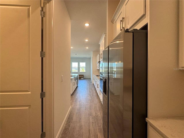 kitchen with light wood-style flooring, light stone counters, white cabinetry, recessed lighting, and stainless steel fridge