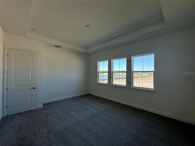 spare room featuring visible vents, dark carpet, a raised ceiling, and baseboards