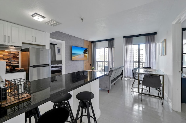 kitchen featuring under cabinet range hood, open floor plan, dark stone countertops, stainless steel appliances, and white cabinetry