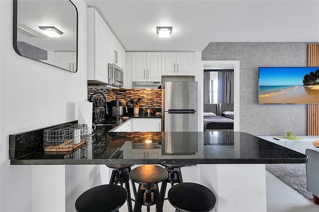 kitchen featuring under cabinet range hood, tasteful backsplash, white cabinetry, appliances with stainless steel finishes, and a peninsula