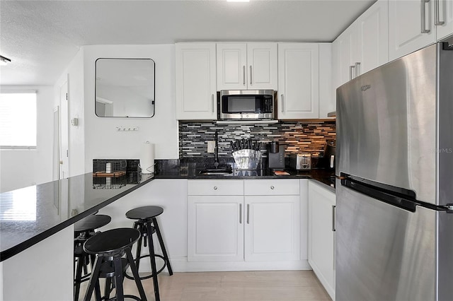 kitchen featuring backsplash, a kitchen breakfast bar, stainless steel appliances, white cabinets, and a textured ceiling