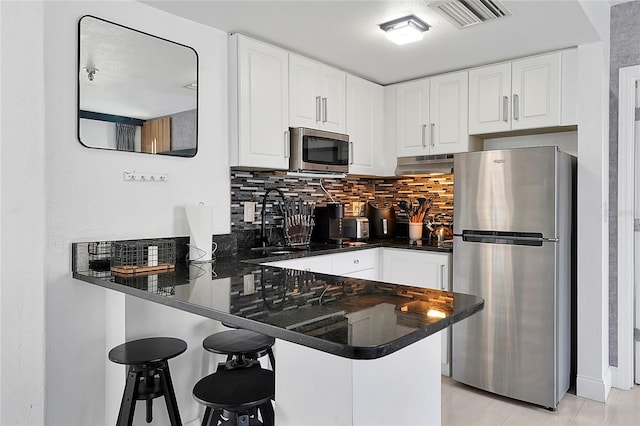 kitchen featuring under cabinet range hood, appliances with stainless steel finishes, a peninsula, and white cabinets