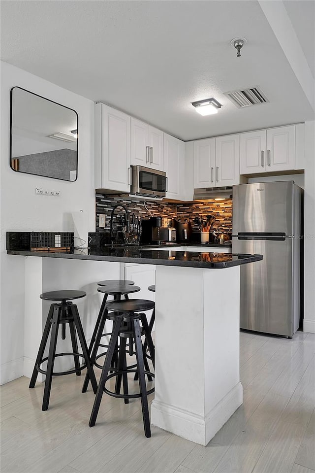 kitchen with visible vents, a peninsula, appliances with stainless steel finishes, under cabinet range hood, and dark countertops