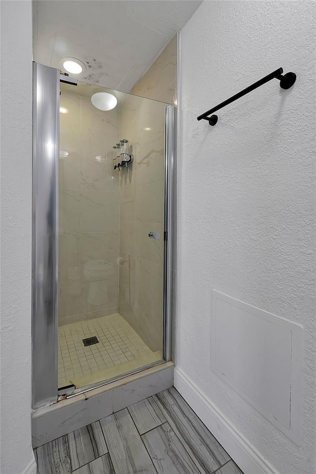 full bathroom featuring a stall shower, baseboards, and a textured wall