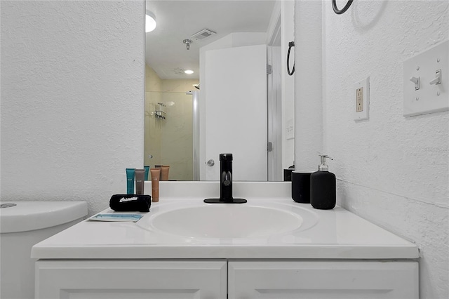 bathroom with visible vents, vanity, a shower stall, and a textured wall