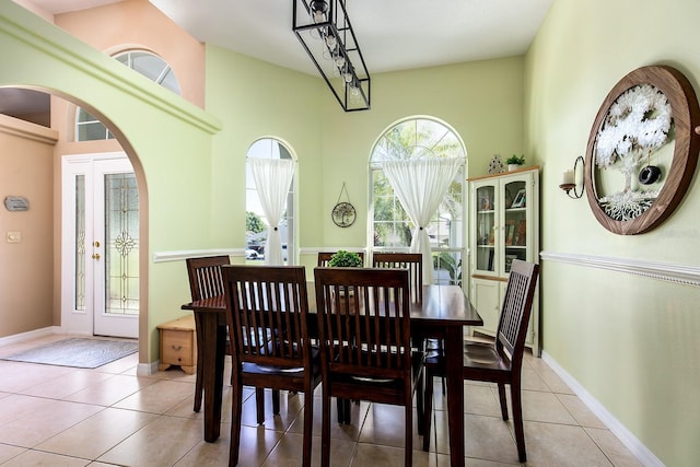 dining space featuring light tile patterned floors, arched walkways, baseboards, and a towering ceiling