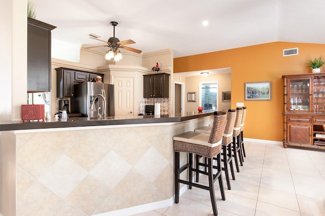 kitchen with dark brown cabinetry, a kitchen breakfast bar, stainless steel refrigerator with ice dispenser, light tile patterned flooring, and a ceiling fan