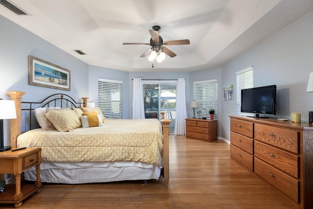 bedroom featuring light wood-type flooring, visible vents, a raised ceiling, and access to outside