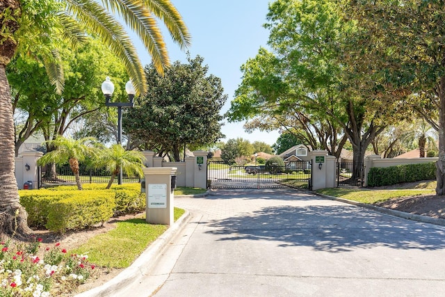 view of road with a gated entry, curbs, street lights, and a gate