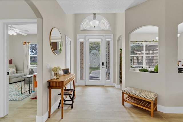 entryway with a wealth of natural light, arched walkways, a textured ceiling, and a ceiling fan