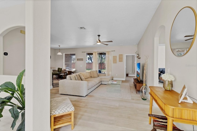 living area with visible vents, arched walkways, light wood finished floors, baseboards, and ceiling fan