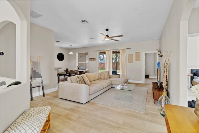 living area with light wood-style floors, a ceiling fan, arched walkways, and baseboards