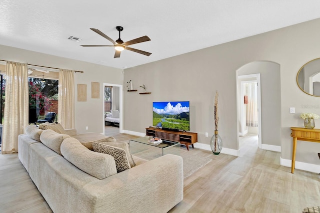 living area featuring visible vents, arched walkways, light wood-style floors, baseboards, and ceiling fan