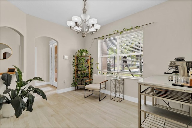 sitting room featuring arched walkways, baseboards, light wood-type flooring, and an inviting chandelier