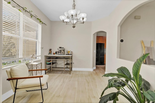 living area with light wood-style flooring, a notable chandelier, baseboards, and arched walkways