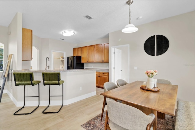 dining space featuring visible vents, arched walkways, baseboards, and light wood finished floors