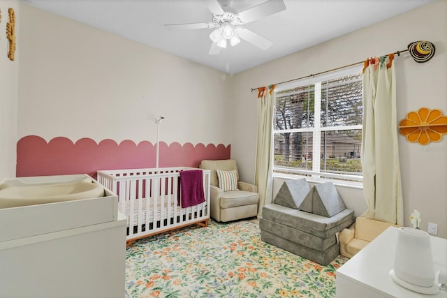 carpeted bedroom with a nursery area and a ceiling fan