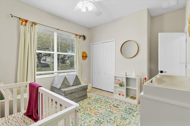 bedroom featuring visible vents, a nursery area, wood finished floors, a closet, and a ceiling fan