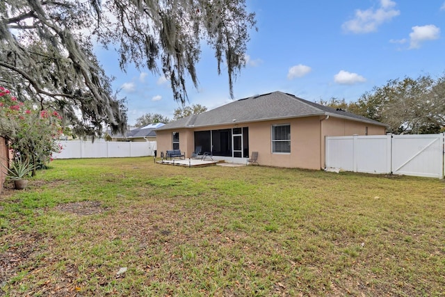 rear view of property with a patio, a yard, a fenced backyard, a sunroom, and stucco siding